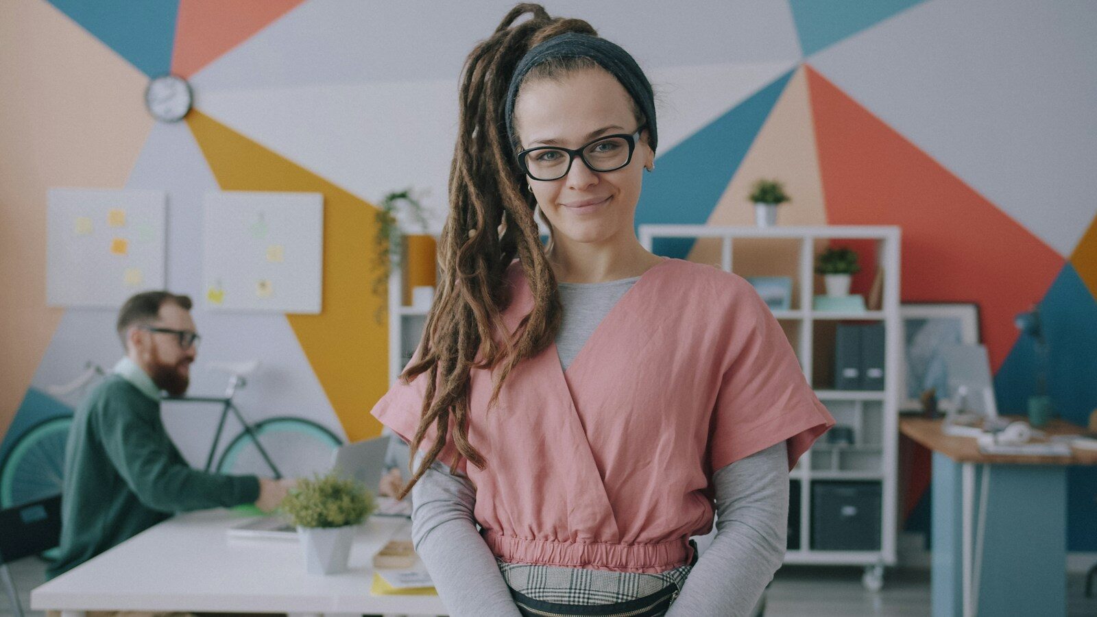 A woman with dreadlocks and glasses in a pink top in a colorful office